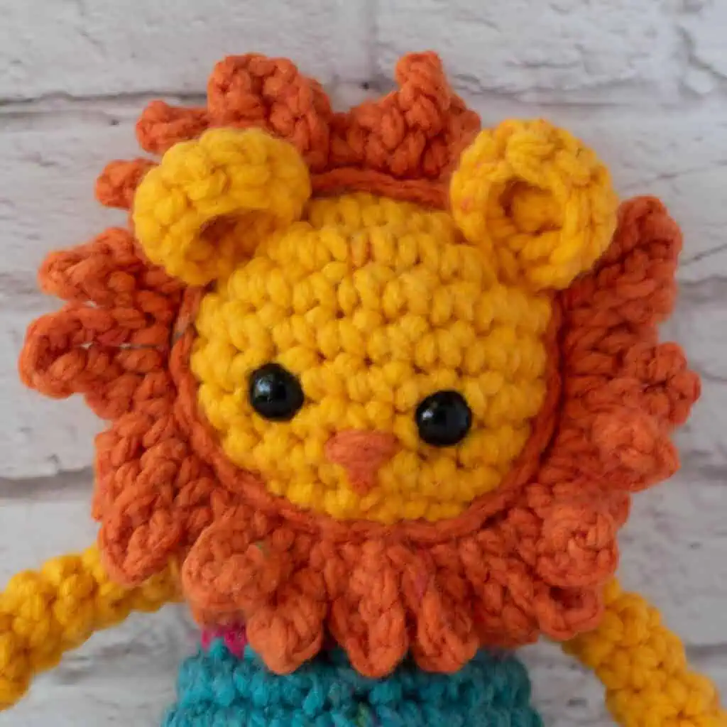 Close up of crochet lion face in yellow, orange and blue yarn